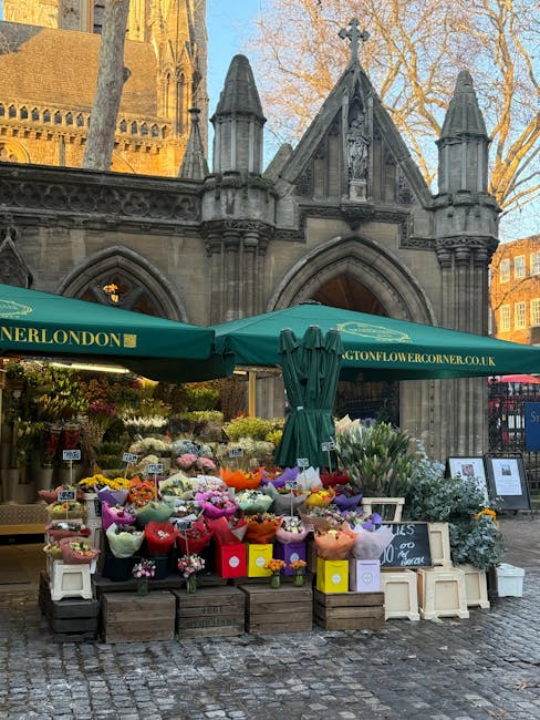 A vibrant outdoor flower stall situated in front of a historic stone church with Gothic architectural features, including pointed arches and decorative pinnacles, in an urban setting with leafless tre