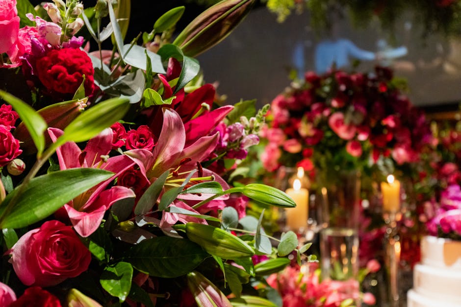 A close-up view of a floral arrangement featuring pink lilies, deep pink roses, and small pink blossoms, complemented by green foliage and eucalyptus leaves. The flowers are arranged in a lush, dense