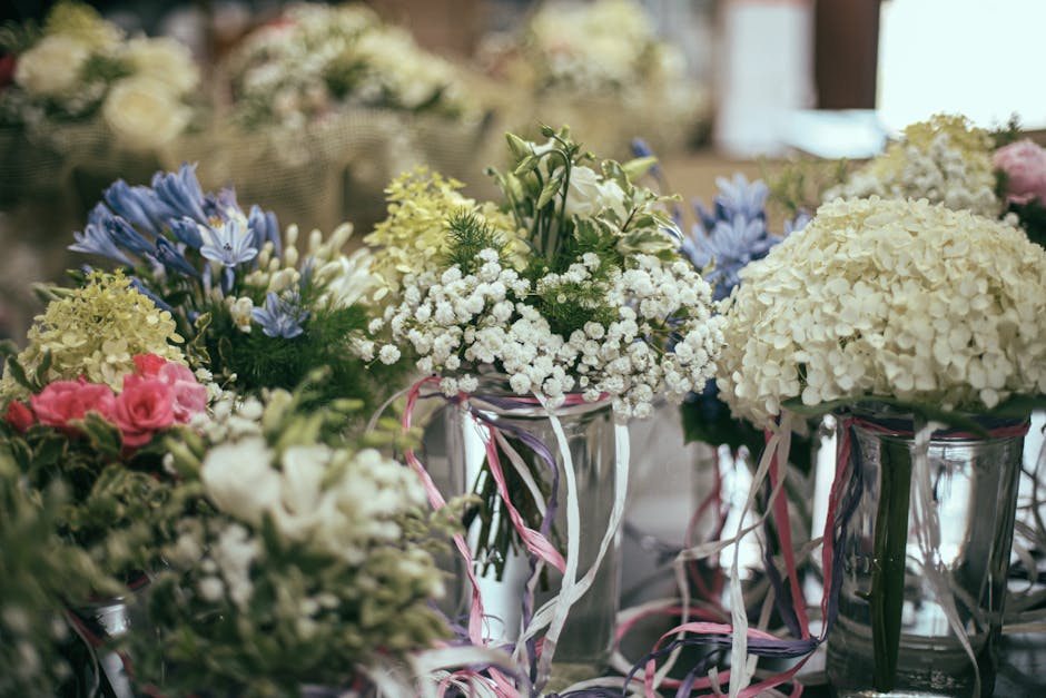 A collection of floral arrangements featuring a variety of fresh flowers displayed in glass vases, including large white hydrangeas, delicate white baby's breath, light pink roses, and blue flowers wi
